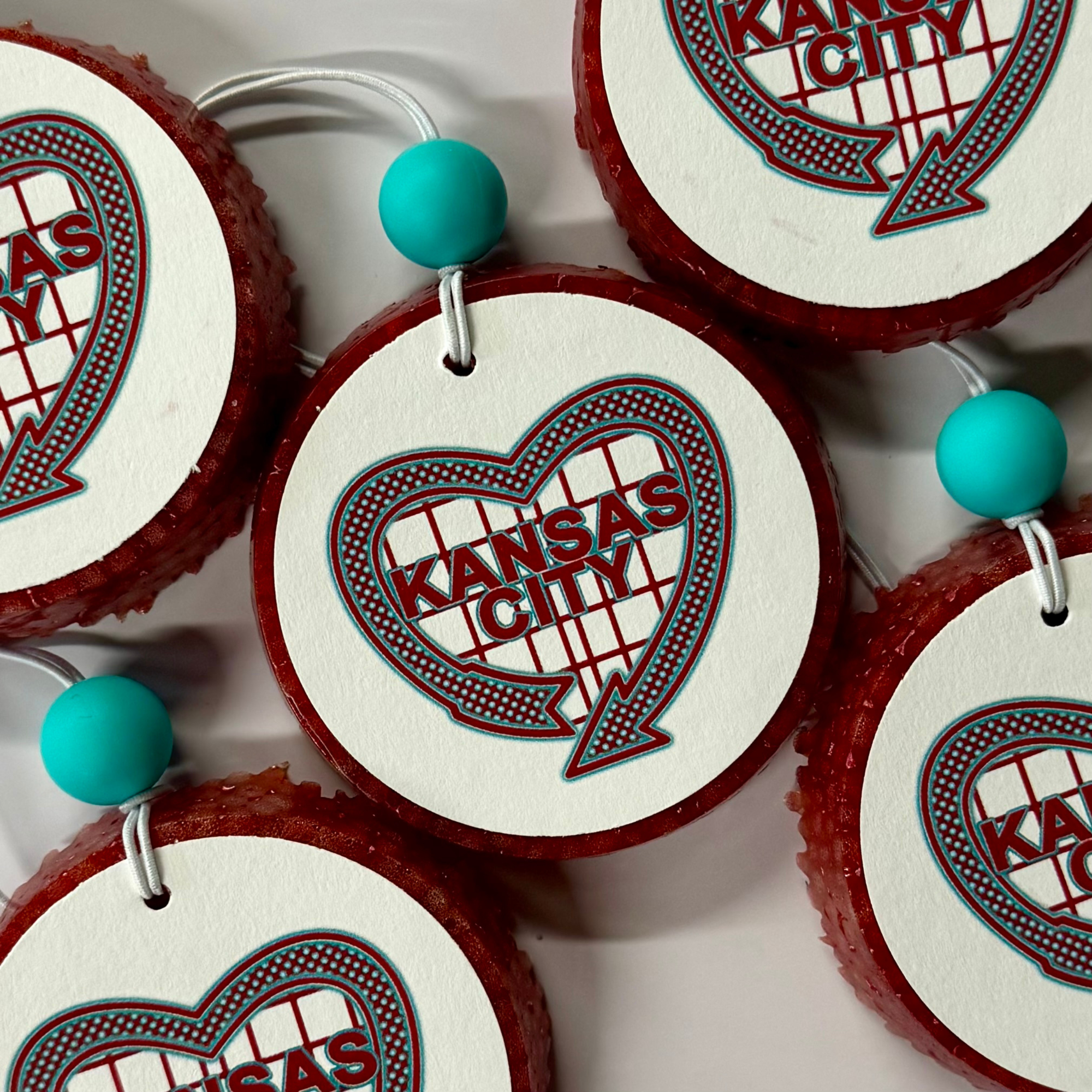 Red and white circular air freshener with 'Kansas City' text and turquoise beads on a white background