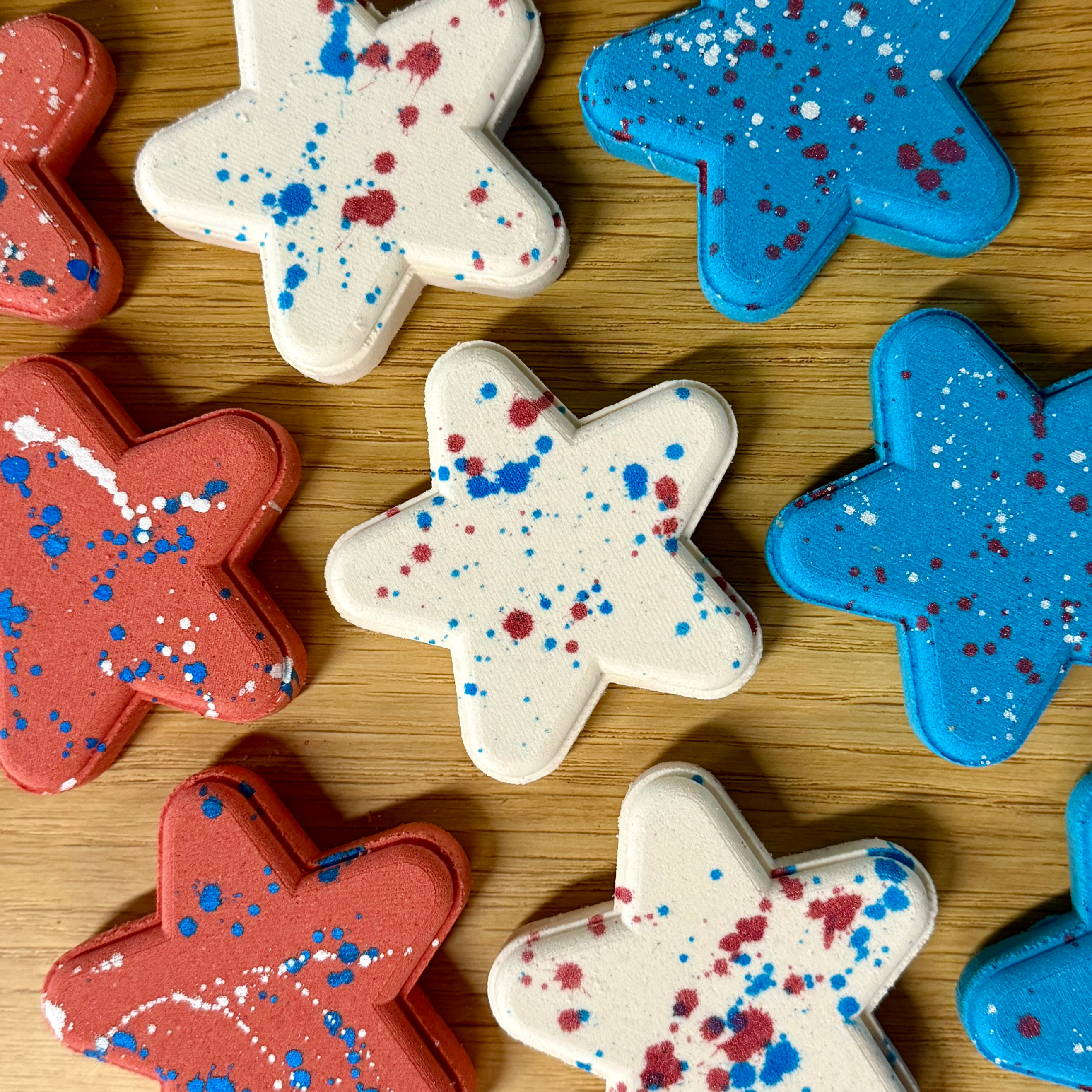 Star-shaped bath bombs with red, white, and blue sprinkles on a wooden surface