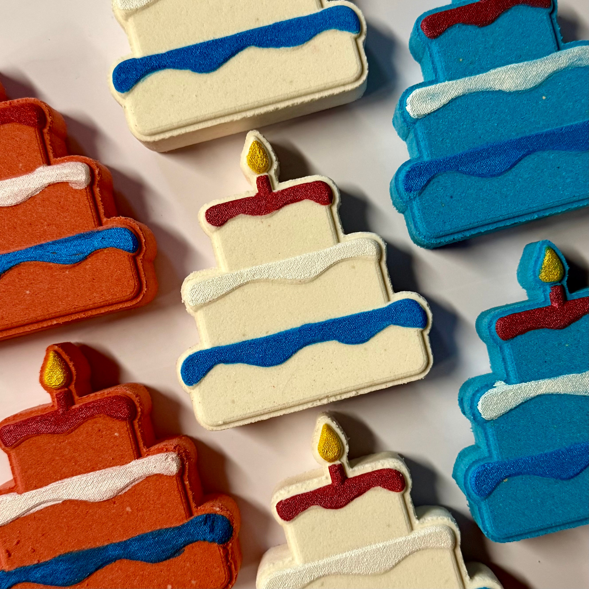 Colorful cake-shaped bath bombs with candles on a light background