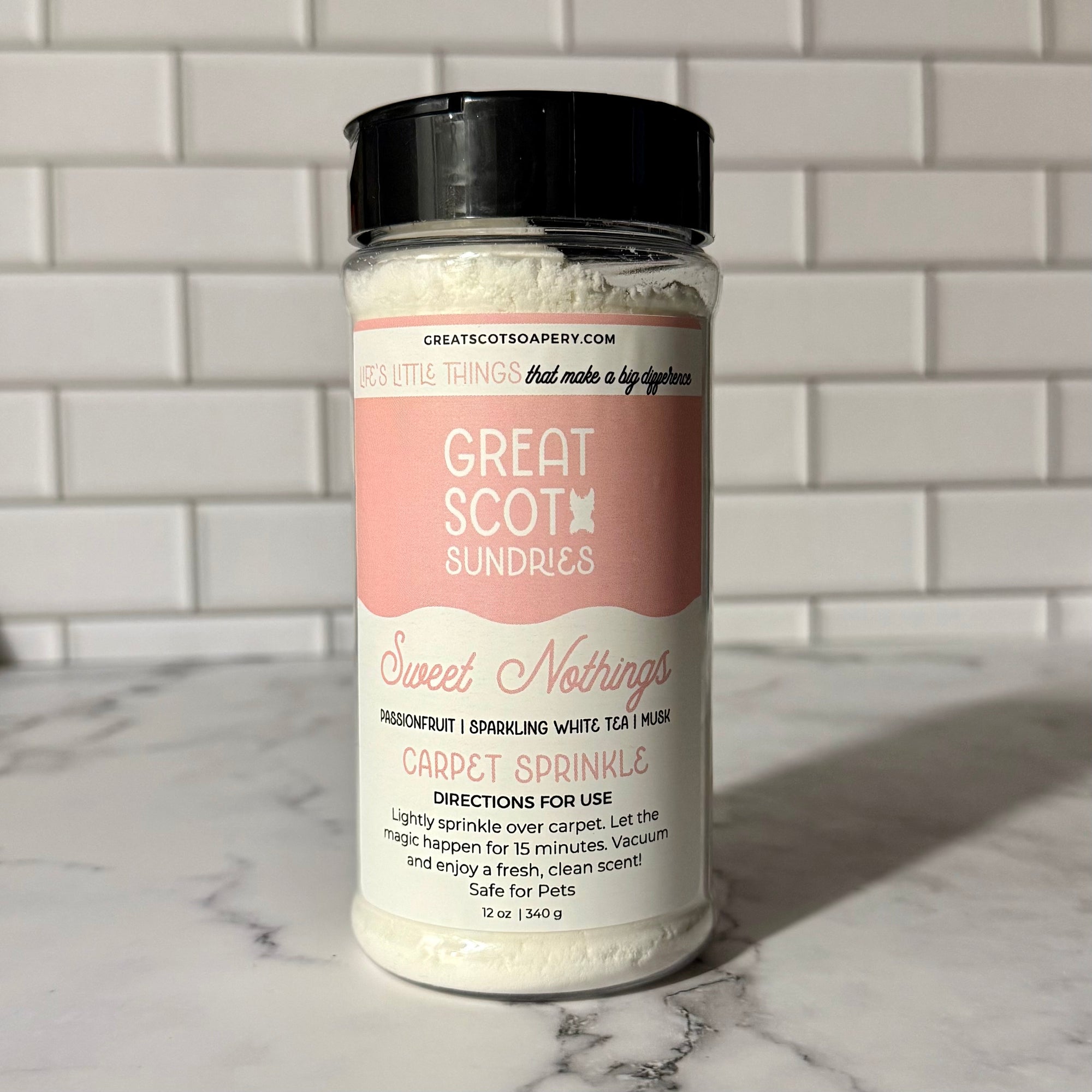 Bottle of 'Sweet Nothings' carpet sprinkle by Great Scot Sundries on a marble surface with a tiled wall background.