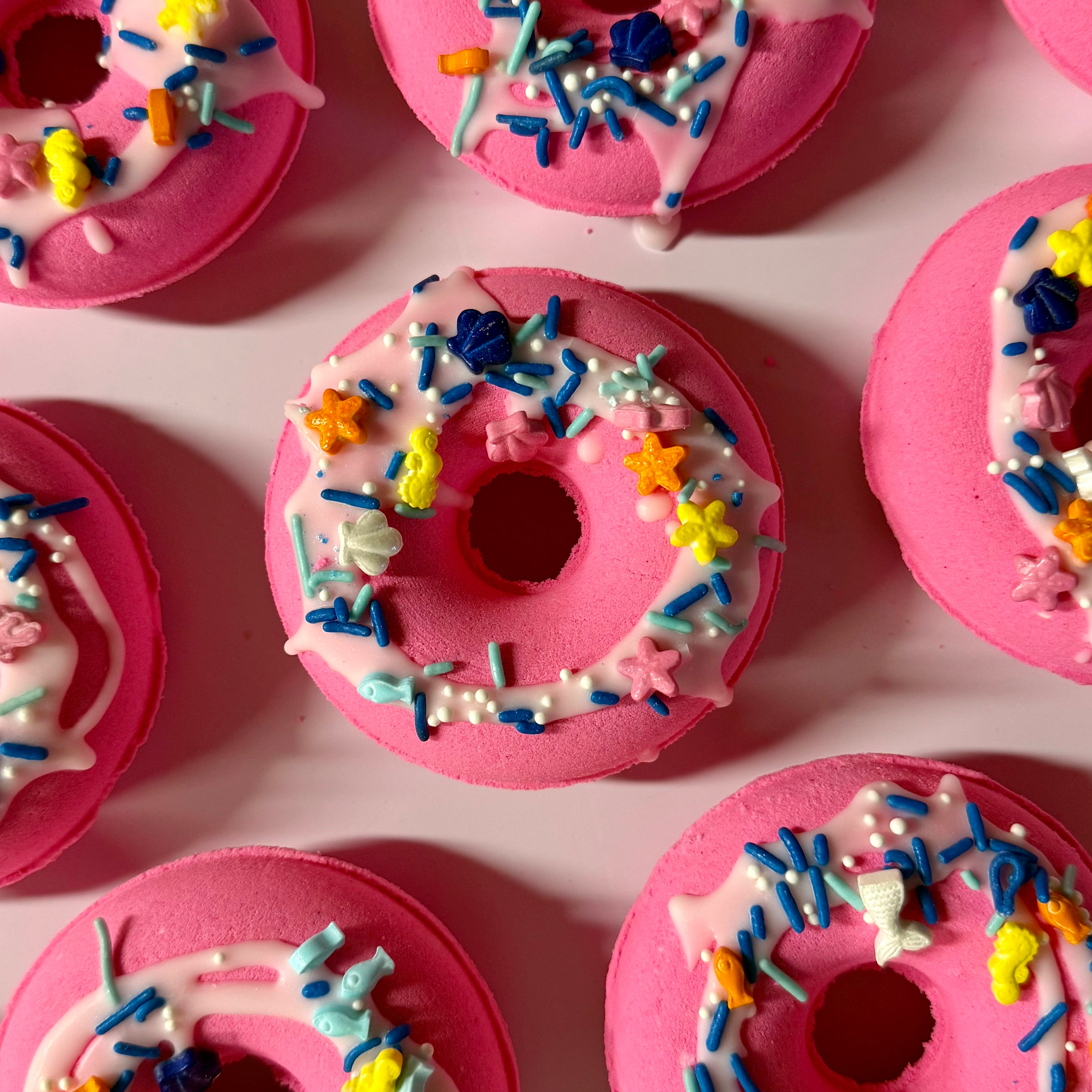 Pink donut bath bomb with colorful sprinkles arranged on a pink background
