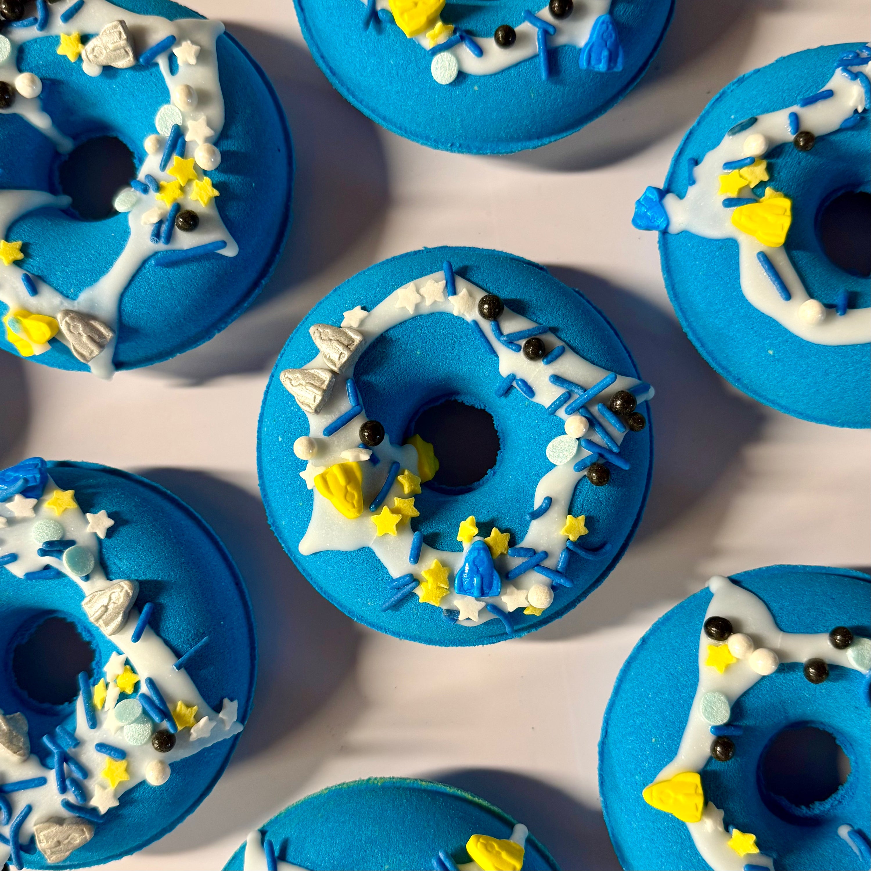 Blue donut bath bombs with white icing and decorative elements on a light pink background