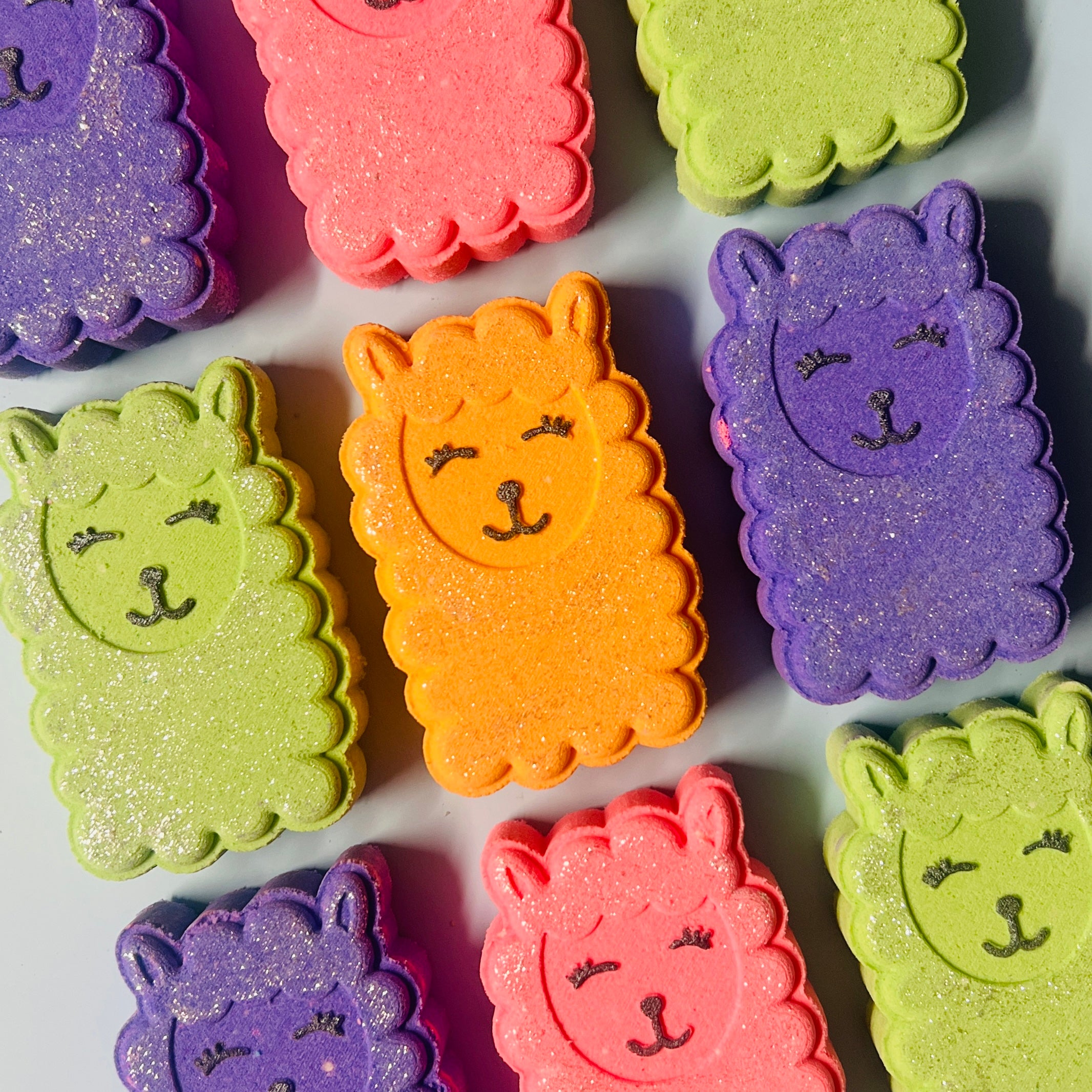 Colorful llama-shaped bath bombs on a white background