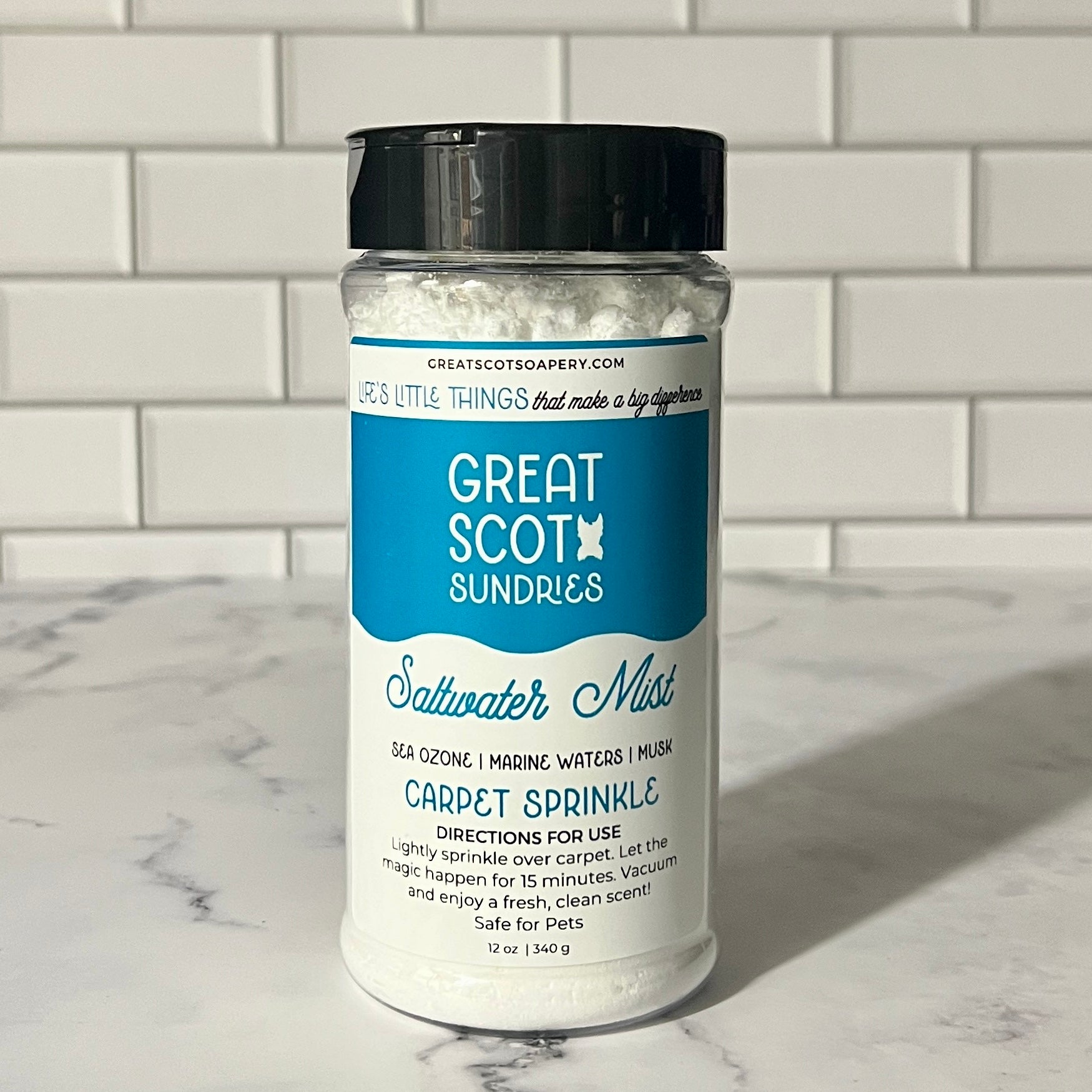 Jar of 'Great Scot! Sundries' saltwater mist carpet sprinkle on a marble surface with a tiled wall background.