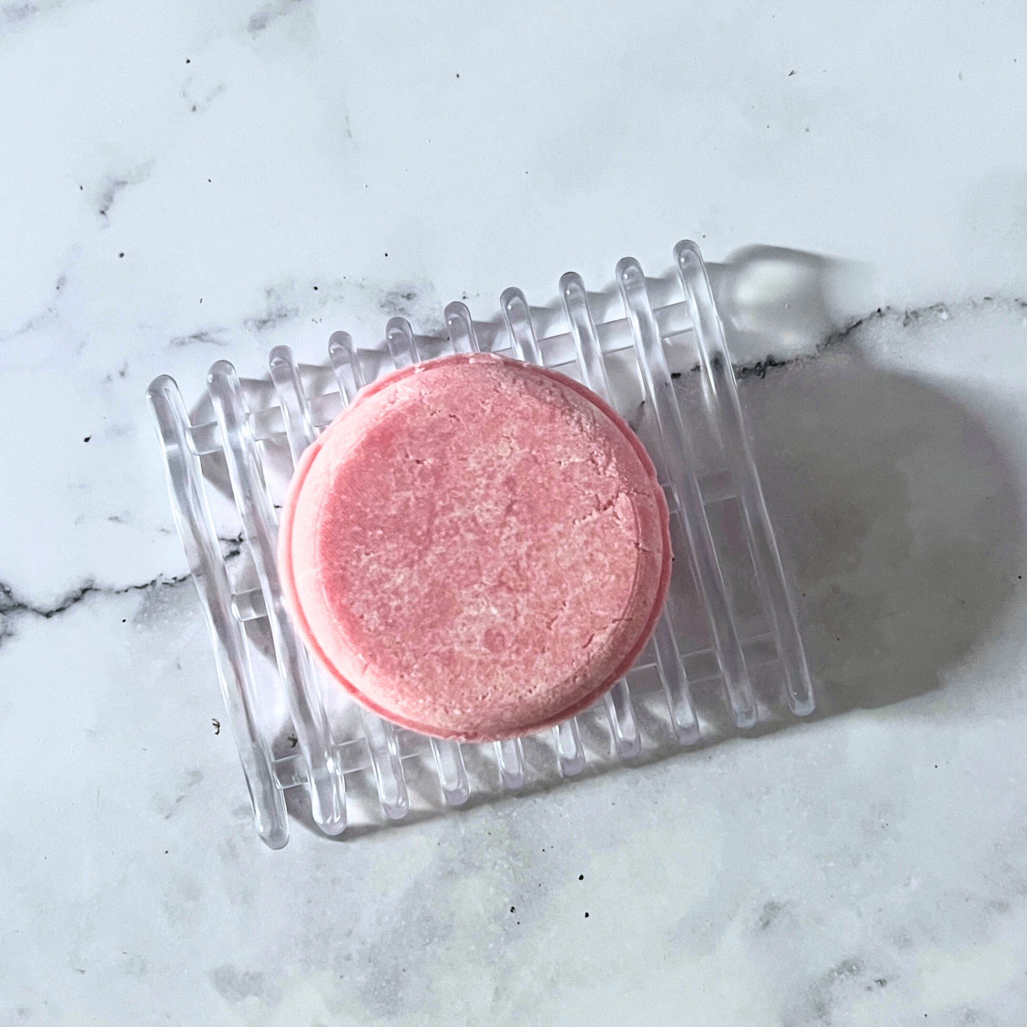 Pink bath bomb on a clear plastic tray on a marble surface