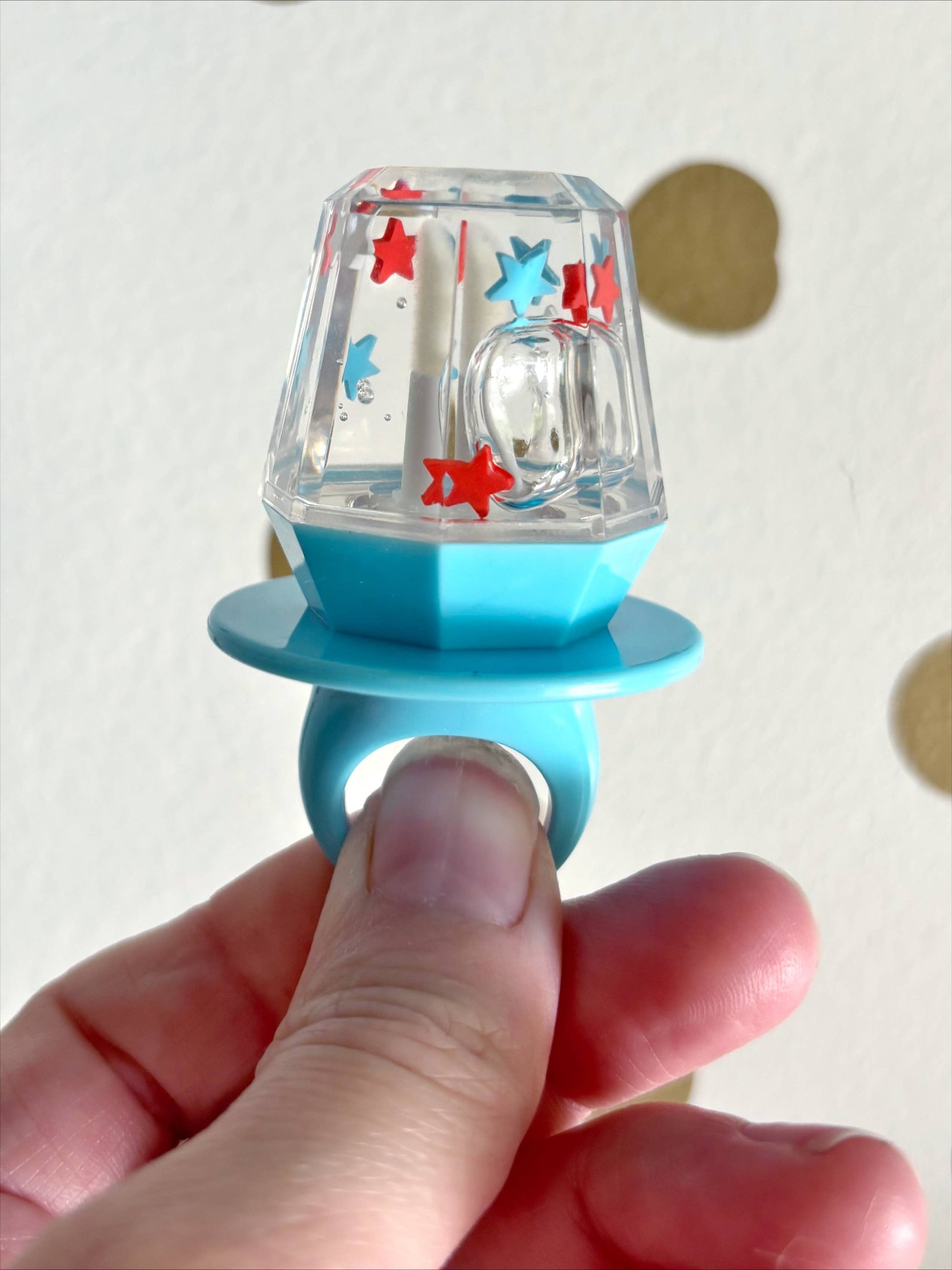 Lip gloss with colorful star design held by a hand against a plain background